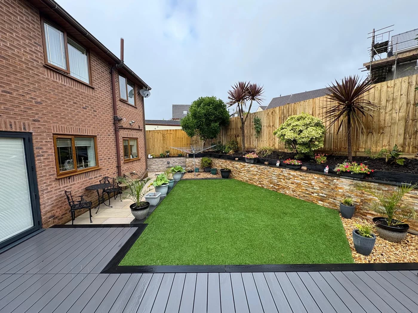 Composite decking, lawn and planted borders in a wide garden view in Bridgend by HJB