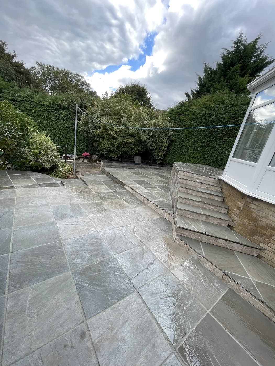 Sandstone patio beside a conservatory in a rear garden in Maesteg by HJB